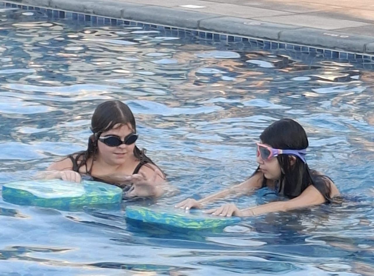 Two swimmers in goggles holding kickboards at the edge of a pool
